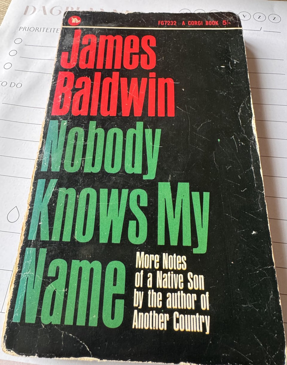 Een oude, beduimelde Corgi-pocket van Nobody Knows My Name van James Baldwin, liggend op een dagplanner.